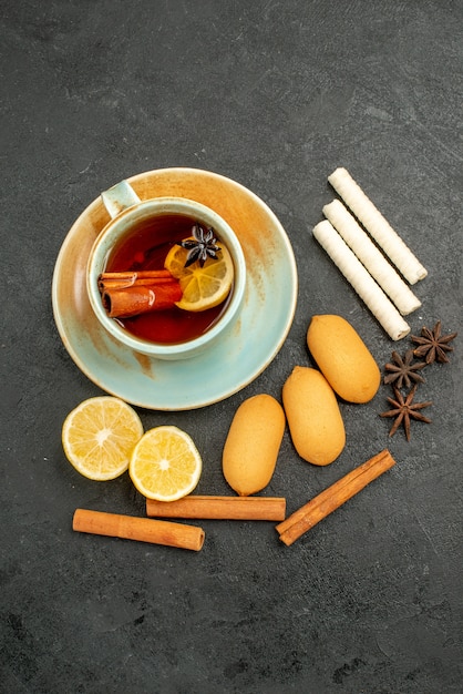 Vista dall'alto tazza di tè con limone e biscotti sulla scrivania scura