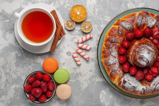 Vista dall'alto tazza di tè con macarons e torta di fragole su superficie bianco chiaro