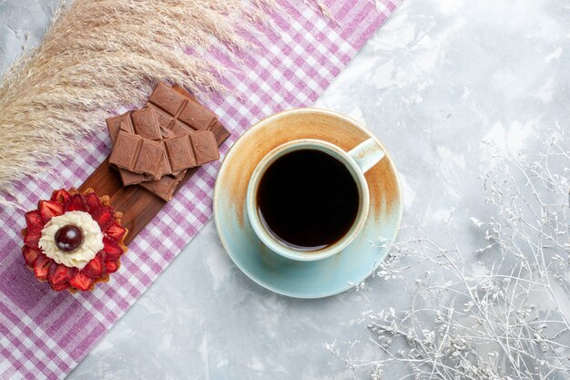 Vista dall'alto tazza di tè con torta e barrette di cioccolato sulla scrivania bianca torta di zucchero dolce al cioccolato