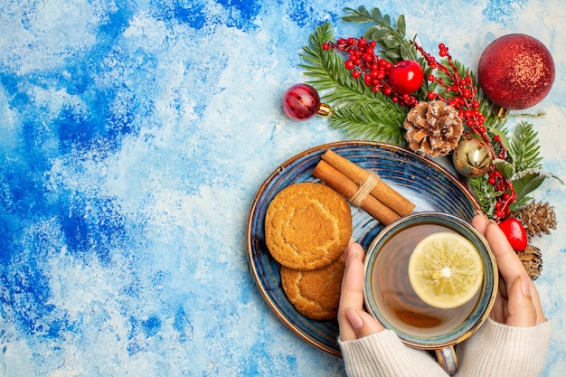 Vista dall'alto tazza di tè fette di limone bastoncini di cannella biscotti nel piattino sul tavolo blu con spazio libero