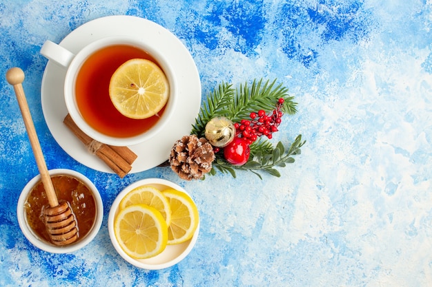 Vista dall'alto tazza di tè miele in ciotola fette di limone rami di albero di Natale sul tavolo blu con spazio libero