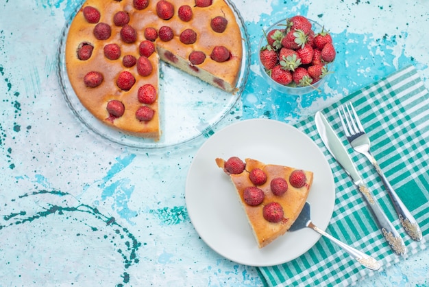 Vista dall'alto torta di fragole a fette e tutta una deliziosa torta insieme a fragole rosse fresche sulla scrivania blu brillante torta ai frutti di bosco dolce cuocere