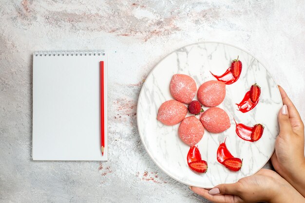 Vista dall'alto torta di fragole rosa piccoli dolci deliziosi sulla torta di biscotto dolce del tè dello zucchero del biscotto dello scrittorio bianco