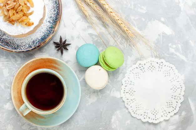 Vista dall'alto torta di zucchero tondo in polvere con tè all'uvetta e macarons su superficie bianca