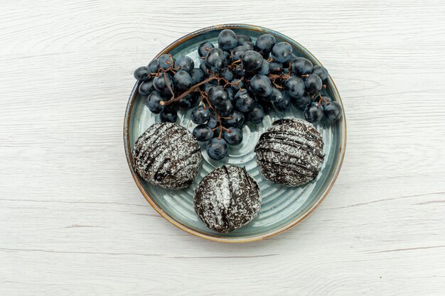 Vista dall'alto torte al cioccolato deliziose con glassa e fresche uve nere su sfondo bianco torta di frutta al cioccolato dolce zucchero fresco biscotto