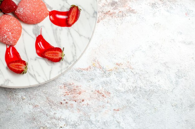 Vista dall'alto torte di fragole rosa piccoli dolci all'interno della piastra su sfondo bianco torta zucchero biscotto biscotto da tè frutta dolce