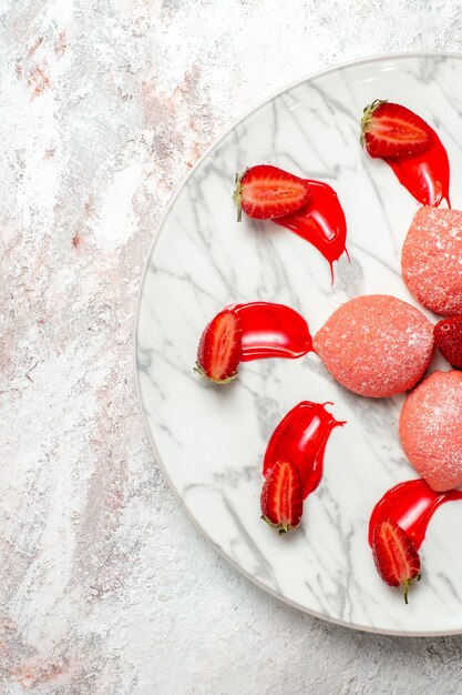 Vista dall'alto torte di fragole rosa piccoli dolci all'interno della piastra su sfondo bianco torta zucchero biscotto biscotto da tè frutta dolce