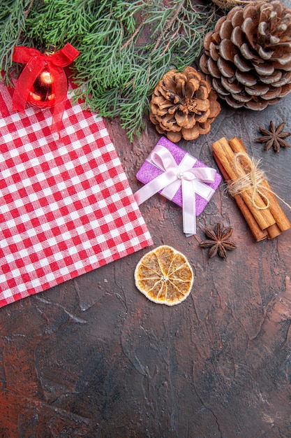 Vista dall'alto tovaglia a quadretti rossa e bianca rami di pino pigne regalo di natale cannella albero di natale palla giocattolo su sfondo rosso scuro spazio libero