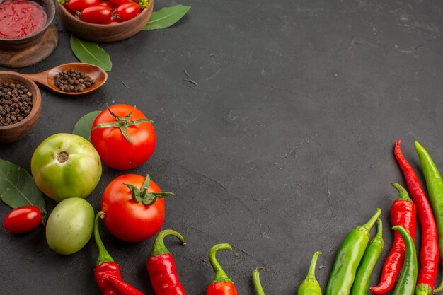 Vista dall'alto una ciotola di pomodorini peperoni rossi e verdi caldi e pomodori foglie di alloro ciotole di ketchup pepe nero e un cucchiaio su fondo nero