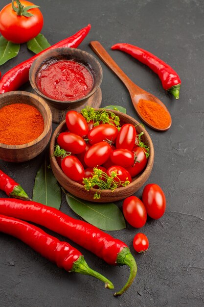 Vista dall'alto una ciotola di pomodorini peperoni rossi piccanti foglie di alloro un cucchiaio di legno ciotole di ketchup e peperoncino piccante in polvere e pomodoro sul lato sinistro della terra nera