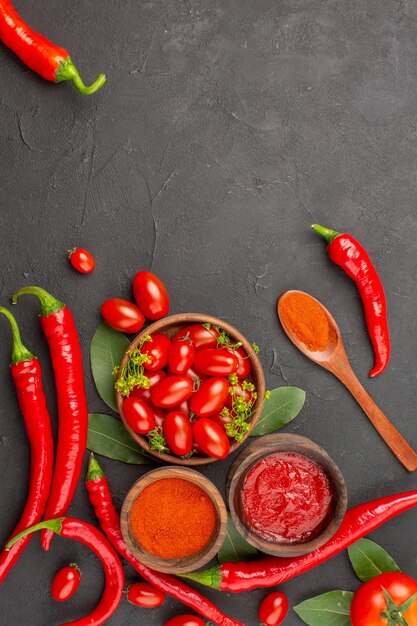 Vista dall'alto una ciotola di pomodorini peperoni rossi piccanti un cucchiaio di legno foglie di alloro ciotole di ketchup e polvere di peperoncino e pomodoro sul fondo della terra nera