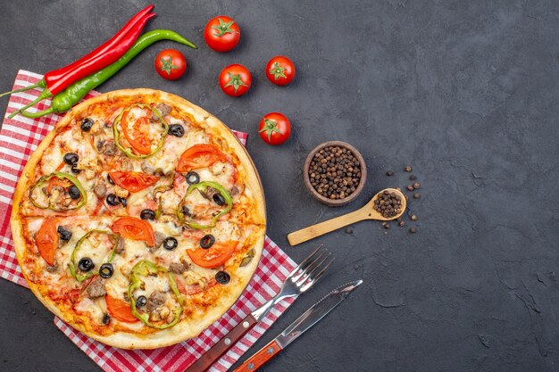 Vista dall'alto una deliziosa pizza al formaggio con olive, pepe e pomodori sulla superficie scura