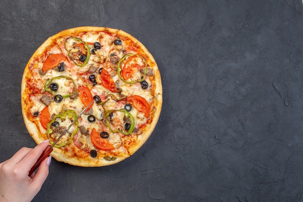 Vista dall'alto una deliziosa pizza al formaggio con olive, pepe e pomodori sulla superficie scura