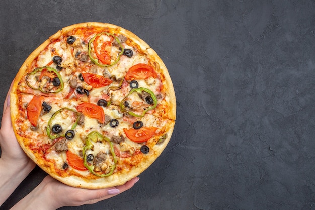 Vista dall'alto una deliziosa pizza al formaggio con olive, pepe e pomodori sulla superficie scura