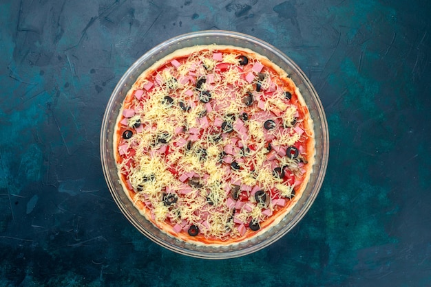 Vista dall'alto una deliziosa pizza al formaggio con olive salsa di pomodoro salsicce all'interno della padella di vetro sulla scrivania azzurra.