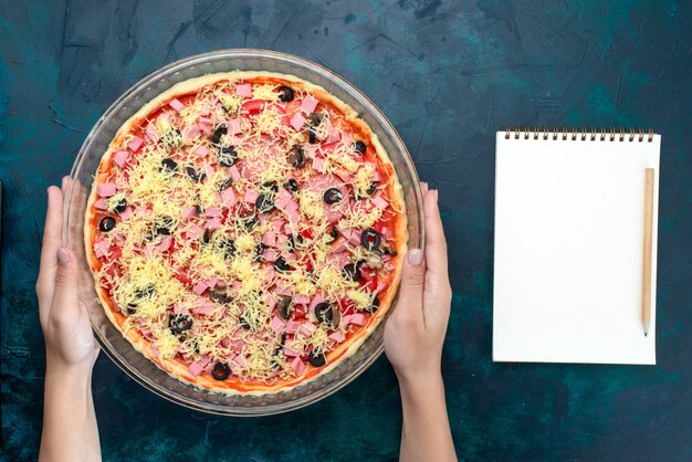 Vista dall'alto una deliziosa pizza al formaggio con olive salsa di pomodoro salsicce all'interno della padella di vetro sulla scrivania azzurra.