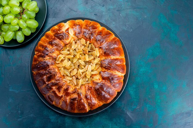 Vista dall'alto una deliziosa torta al forno con uvetta e uva verde fresca su pasta di biscotti dolci con zucchero a torta da scrivania blu scuro