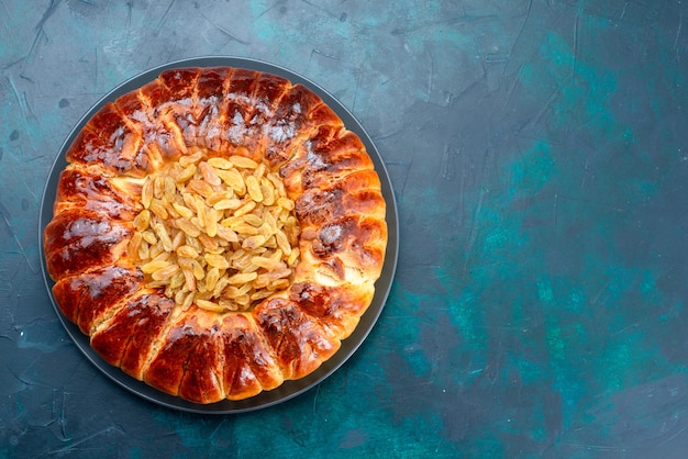 Vista dall'alto una deliziosa torta al forno rotonda dolce formata con uvetta sulla scrivania azzurra.