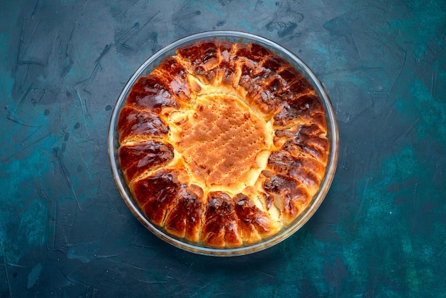 Vista dall'alto una deliziosa torta al forno tonda formata dolce all'interno della teglia di vetro sullo sfondo azzurro.