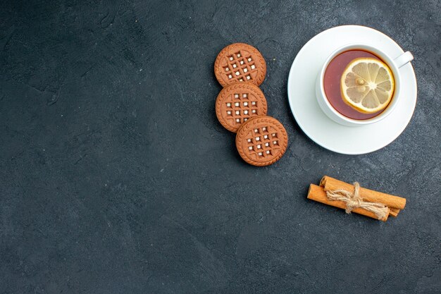 Vista dall'alto una tazza di tè con biscotti al limone e bastoncini di cannella su spazio libero superficie scura