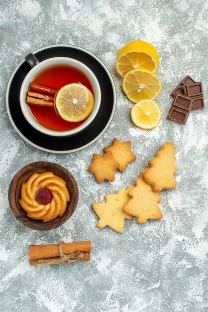 Vista dall'alto una tazza di tè fette di limone bastoncini di cannella biscotti al cioccolato sulla superficie grigia