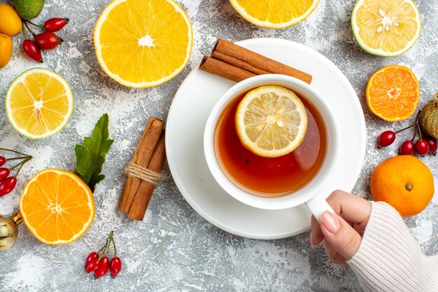 Vista dall'alto una tazza di tè in bastoncini di cannella limoni tagliati a mano femminile su sfondo grigio