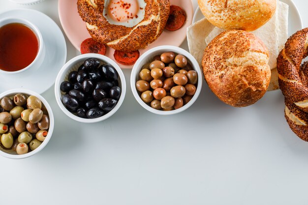 Vista dall'alto uova con salsiccia nel piatto con una tazza di tè, bagel turco, olive, pane sulla superficie bianca