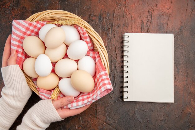 Vista dall'alto uova di gallina bianca all'interno del cesto con asciugamano sul tavolo scuro