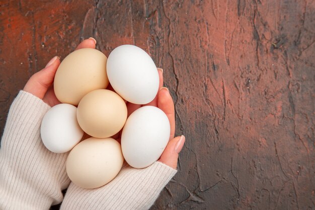 Vista dall'alto uova di gallina bianca all'interno delle mani femminili sul tavolo scuro