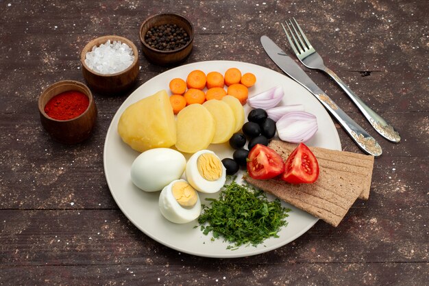 Vista dall'alto Uova sode con olive verdi aglio e pomodori su marrone, colazione pasto di verdure