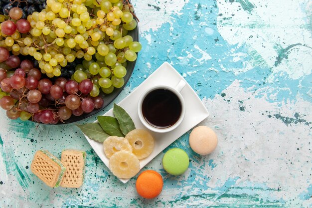 Vista dall'alto uva fresca colorata con tazza di tè macarons e cialde su sfondo azzurro frutta zucchero biscotto torta dolce cuocere torta