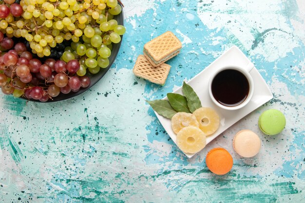 Vista dall'alto uva fresca colorata frutta succosa e pastosa con una tazza di tè sulla superficie azzurra frutti di bosco freschi succhi di frutta vino