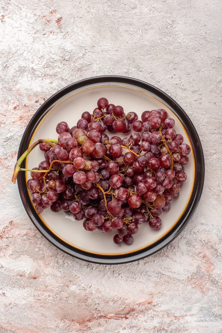 Foto gratuito vista dall'alto uva rossa fresca frutta succosa e pastosa all'interno del piatto su superficie bianca