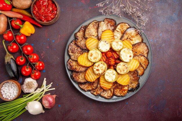 Vista dall'alto verdure al forno patate e melanzane con diversi condimenti su una scrivania buia