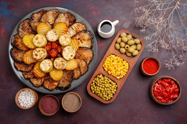 Vista dall'alto verdure al forno patate e melanzane con diversi condimenti su uno spazio buio