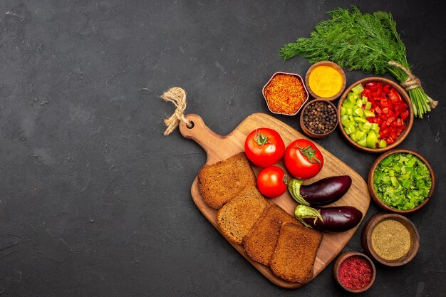 Vista dall'alto verdure fresche con pagnotte di pane scuro e condimenti sulla superficie scura insalata di pane cibo