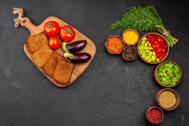 Vista dall'alto verdure fresche con pagnotte di pane scuro e condimenti sulla superficie scura insalata di pane cibo