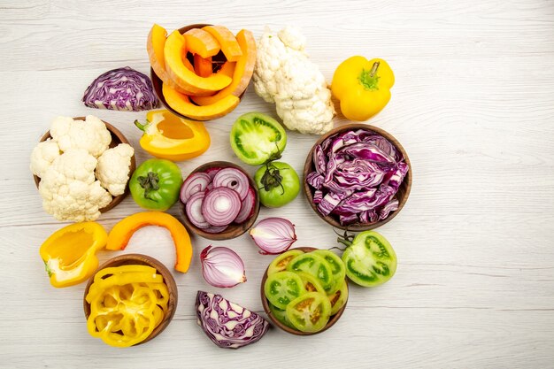 Vista dall'alto verdure fresche tagliate pomodori verdi cavolo rosso cipolla zucca cavolfiore peperone giallo in ciotole su bianco superficie di legno spazio libero