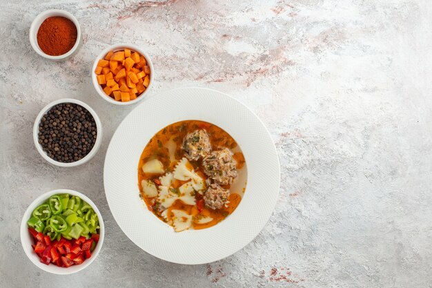 Vista dall'alto zuppa con gustosa zuppa di carne con verdure a fette e diversi condimenti su sfondo bianco