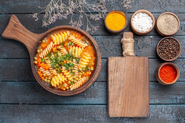 Vista dall'alto zuppa di pasta a spirale pasto delizioso con diversi condimenti sulla cucina di piatto di pasta italiana color zuppa scura da scrivania