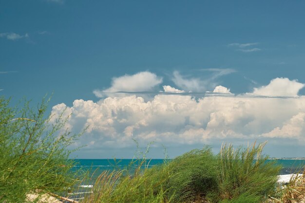 Vista dalle dune di sabbia al mare e al cielo blu con nuvole cumuliformi sfondo del fine settimana estivo per una schermata iniziale o uno sfondo per uno schermo o spazio pubblicitario libero per il testo