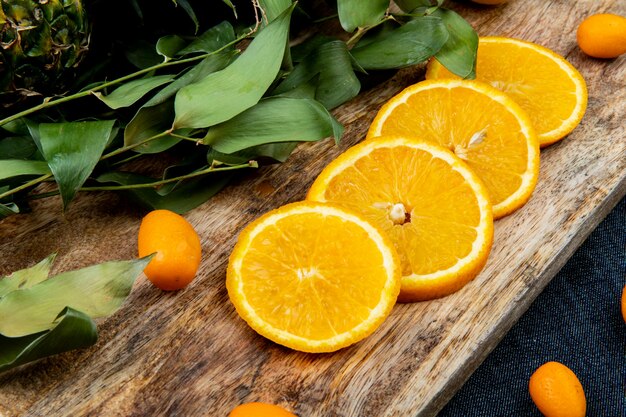 Vista del primo piano degli agrumi come arancia e kumquat con le foglie sul tagliere sul fondo del panno dei jeans