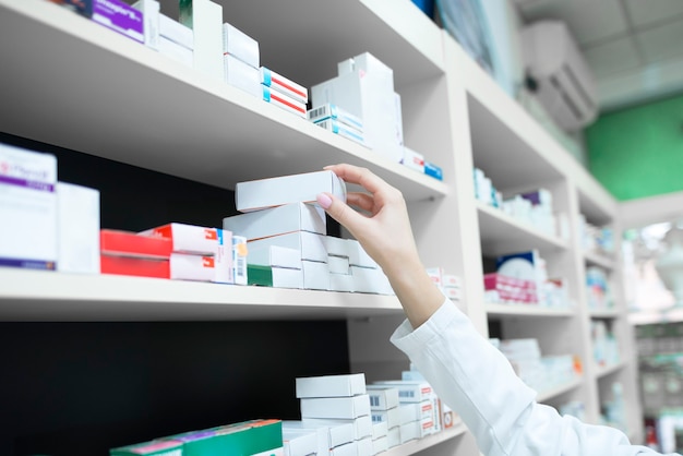 Vista del primo piano della mano del farmacista che prende la scatola della medicina dallo scaffale in drug store