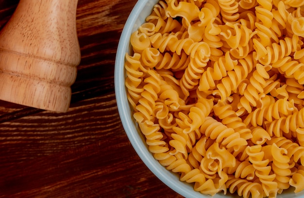 Vista del primo piano della pasta di rotini in ciotola con sale sulla tavola di legno