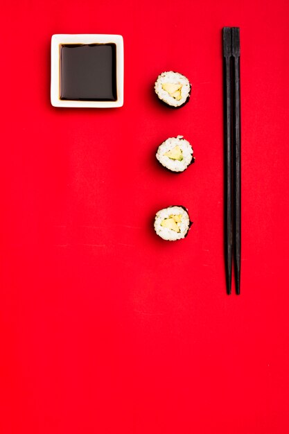 Vista dell&#39;angolo alto dei rotoli di sushi con le bacchette e la salsa di soia sopra fondo rosso
