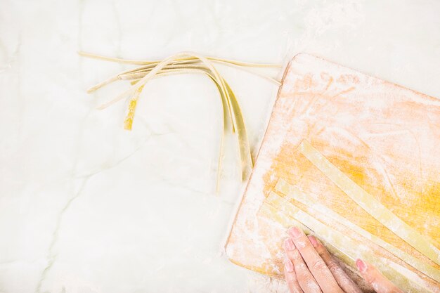 Vista dell&#39;angolo alto della mano della femmina che prepara pasta sul tagliere