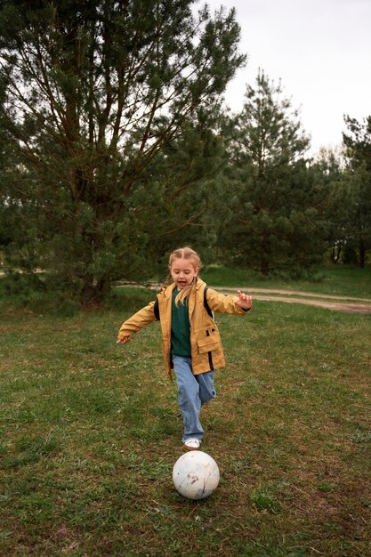 Vista della bambina con lo zaino che si avventura nella natura e gioca a palla