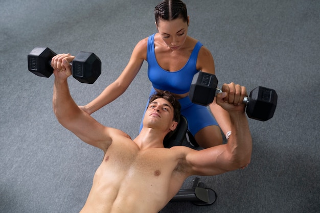 Vista della donna che aiuta l'uomo a fare esercizio in palestra