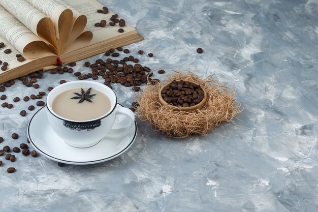 Vista di alto angolo caffè in tazza con chicchi di caffè, libro su sfondo grigio intonaco orizzontale