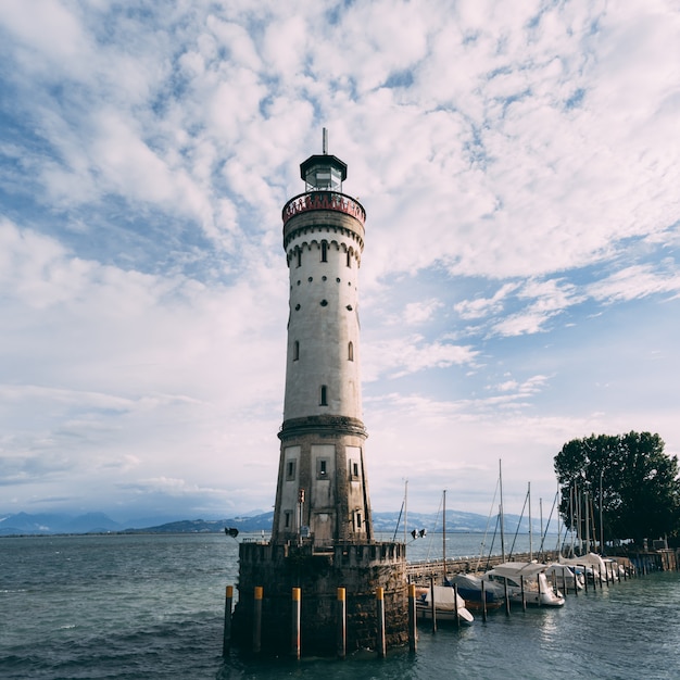 Vista di angolo basso delle navi vicino ad un faro bianco nel mare sotto il bello cielo nuvoloso